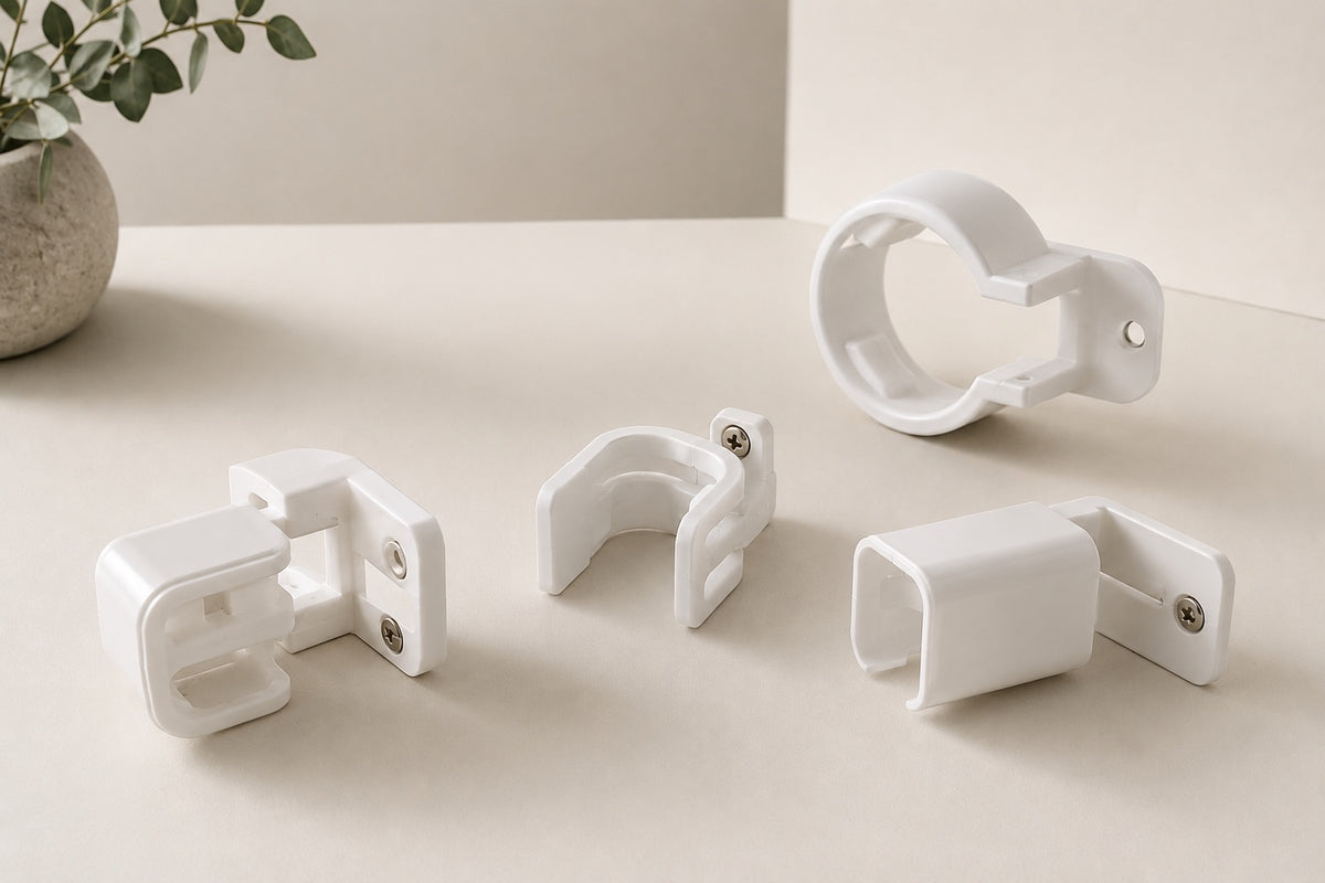 Four white plastic mounting brackets or clips arranged on a light beige surface, with a small potted plant in the background.